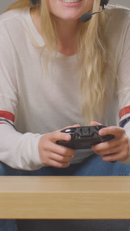 Vertical-Video-Close-Up-Of-Woman-With-Controller-Wearing-Headset-Sitting-On-Sofa-At-Home-Gaming-Online-2